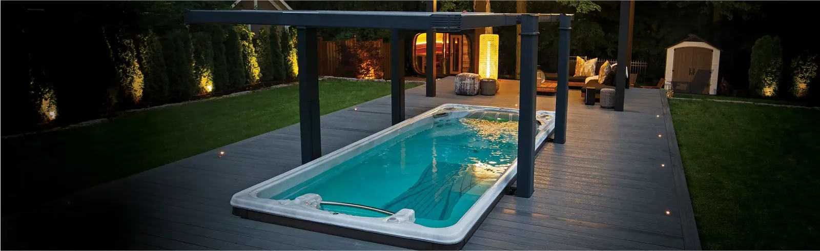 Upplyst Hydropool swimspa på ett trädäck en kväll med trädgårdsbelysning